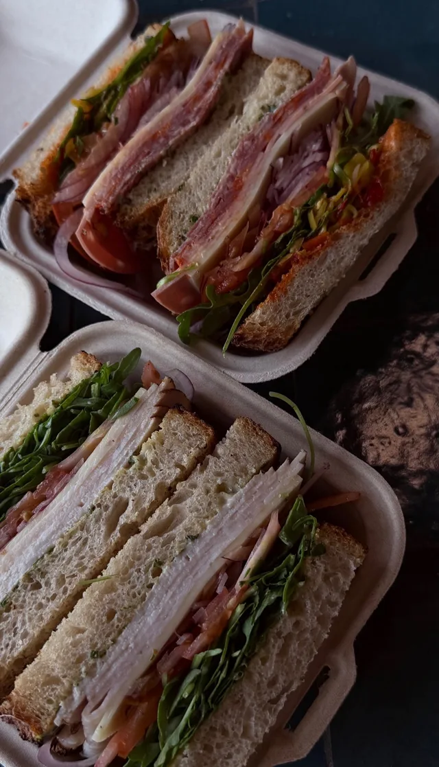 Rooster's sandwiches with deli meats, cheese, and greens in takeout boxes